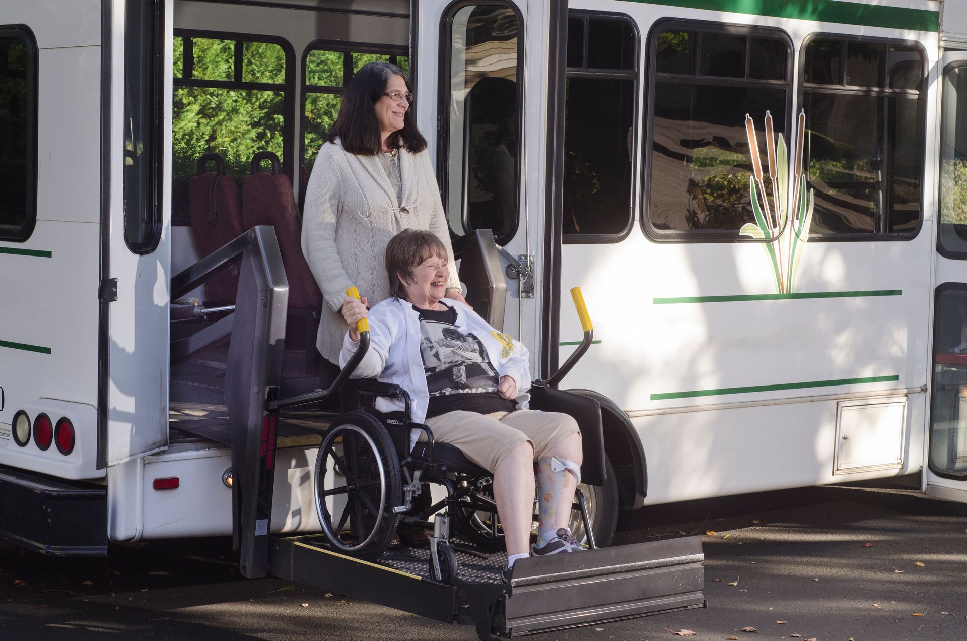 Woman assists wheelchair user boarding a shuttle bus via ramp