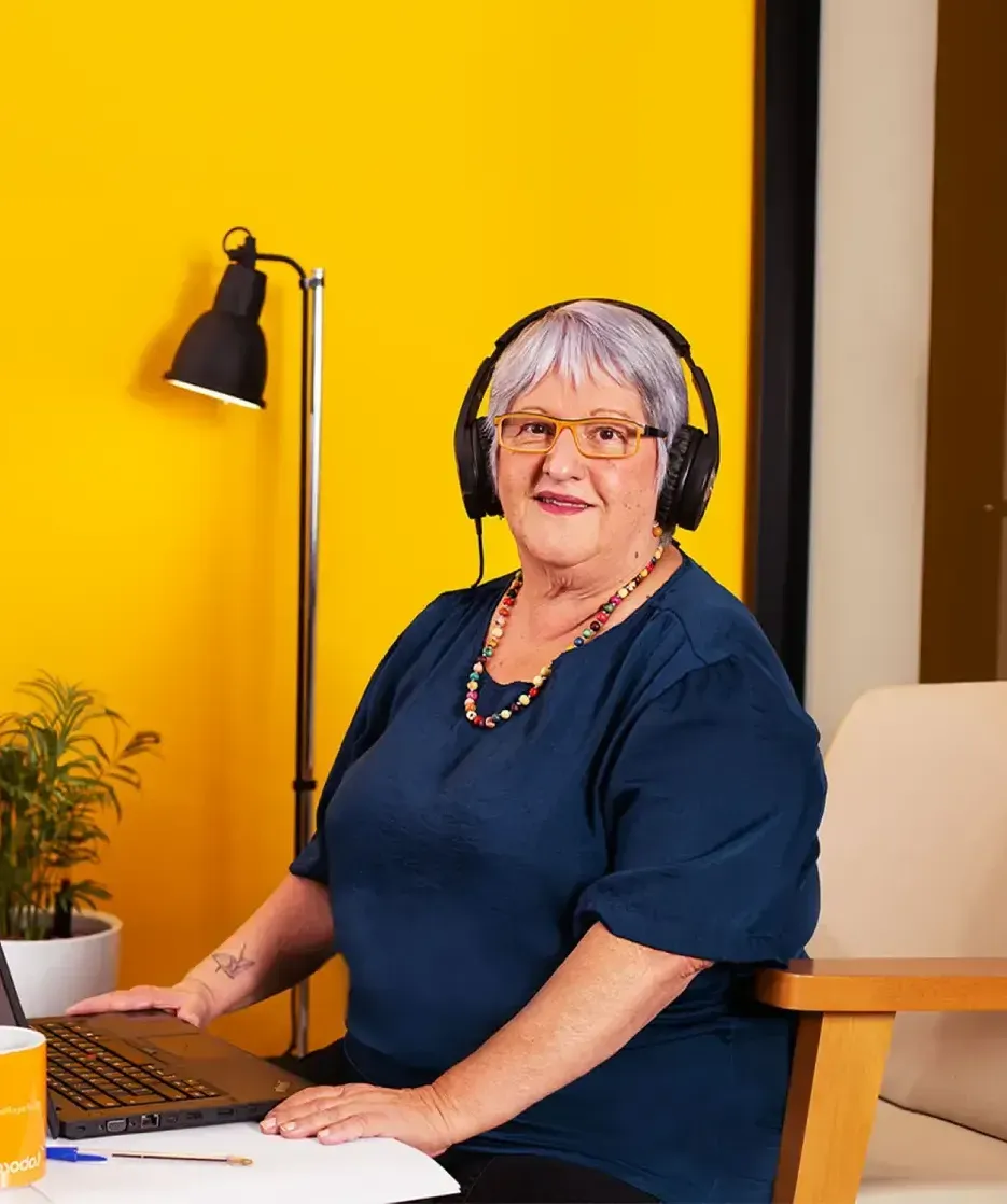 Uma mulher usando fones de ouvido está sentada em uma mesa com um laptop.