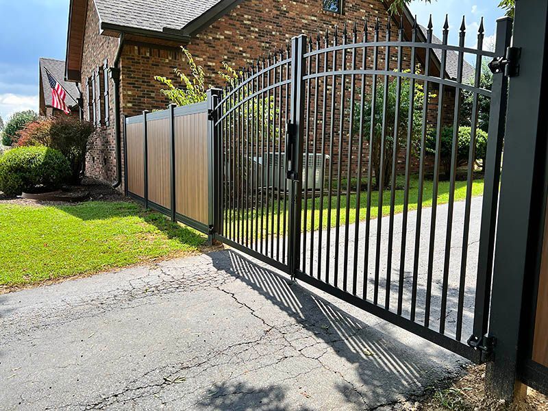 Black metal gate and fence with brown panels in front of a brick house.