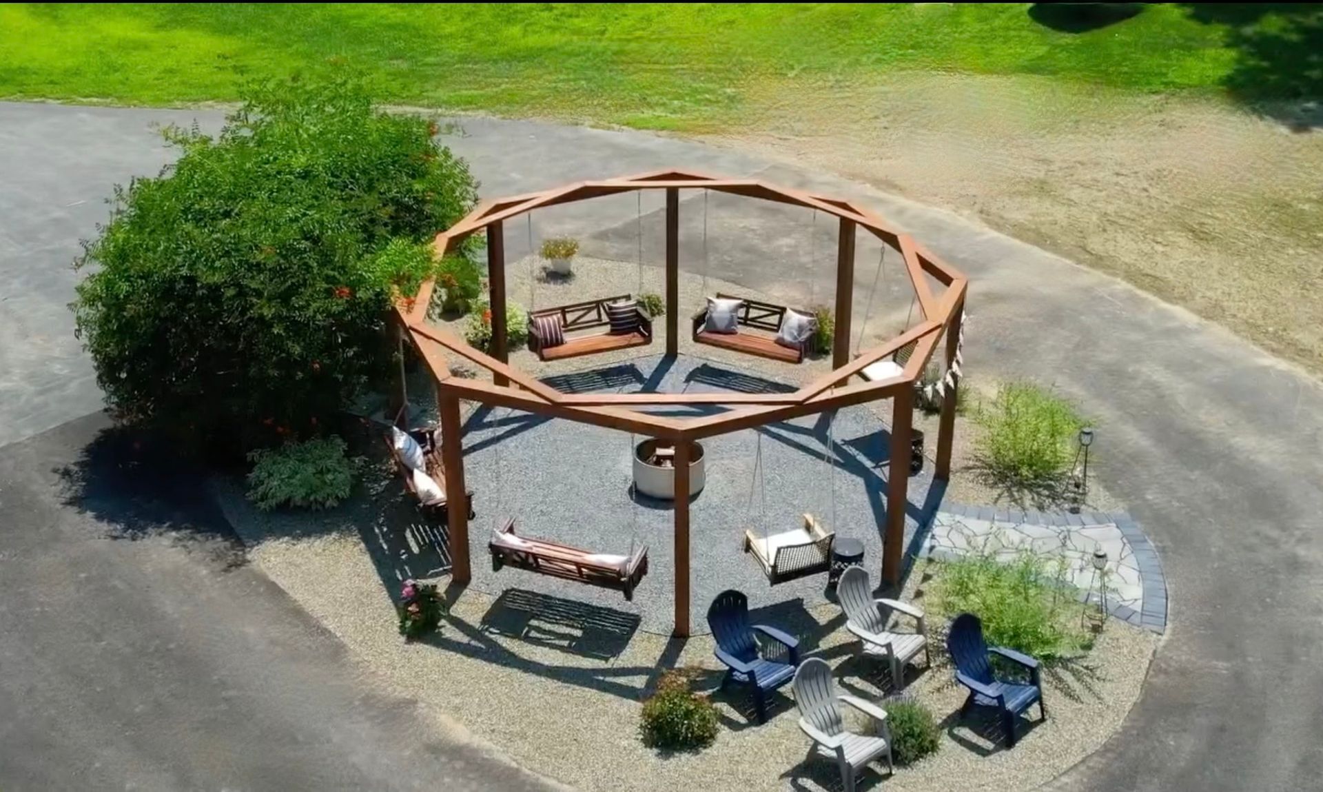 Outdoor seating area with wooden octagon structure holding swings and chairs, surrounding a fire pit.