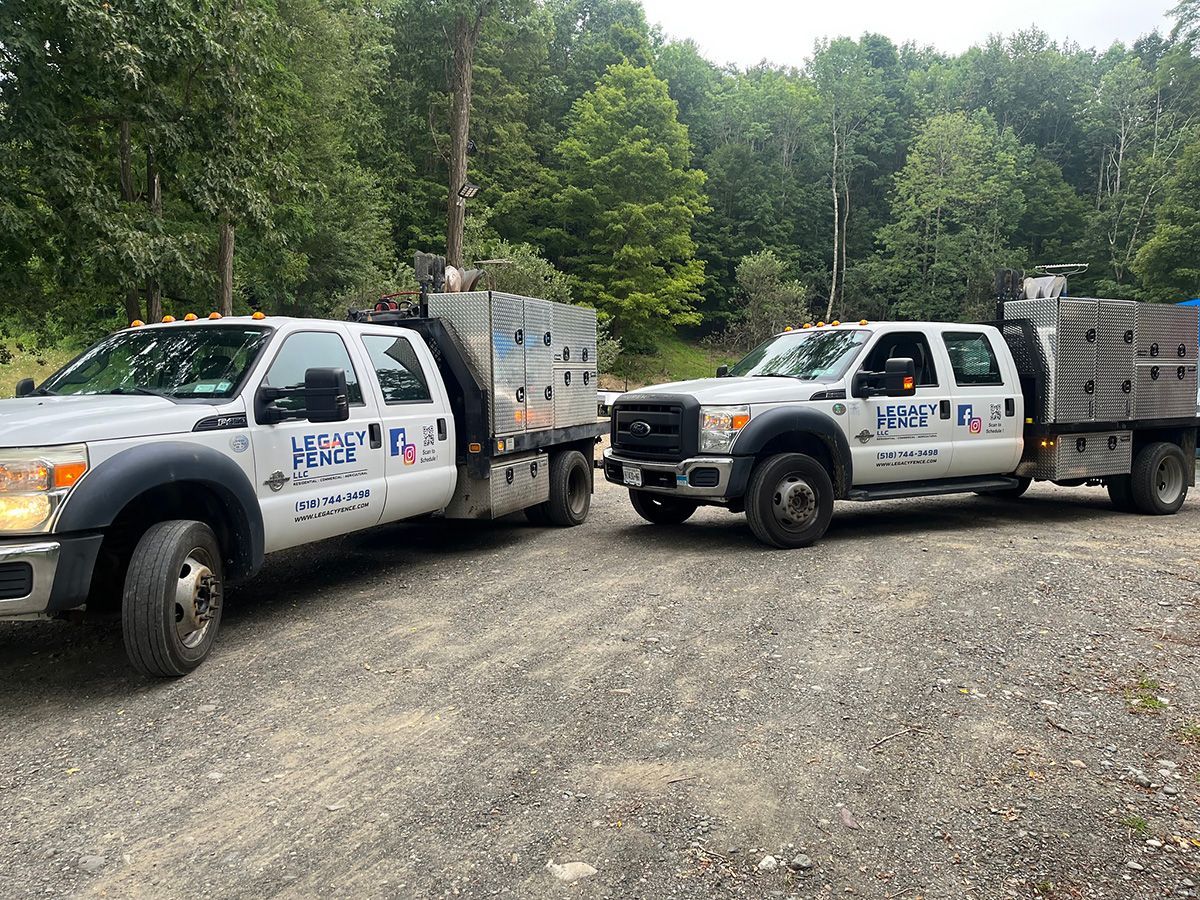 Man stands by a white Legacy Fence truck with toolboxes. Green foliage in the background.