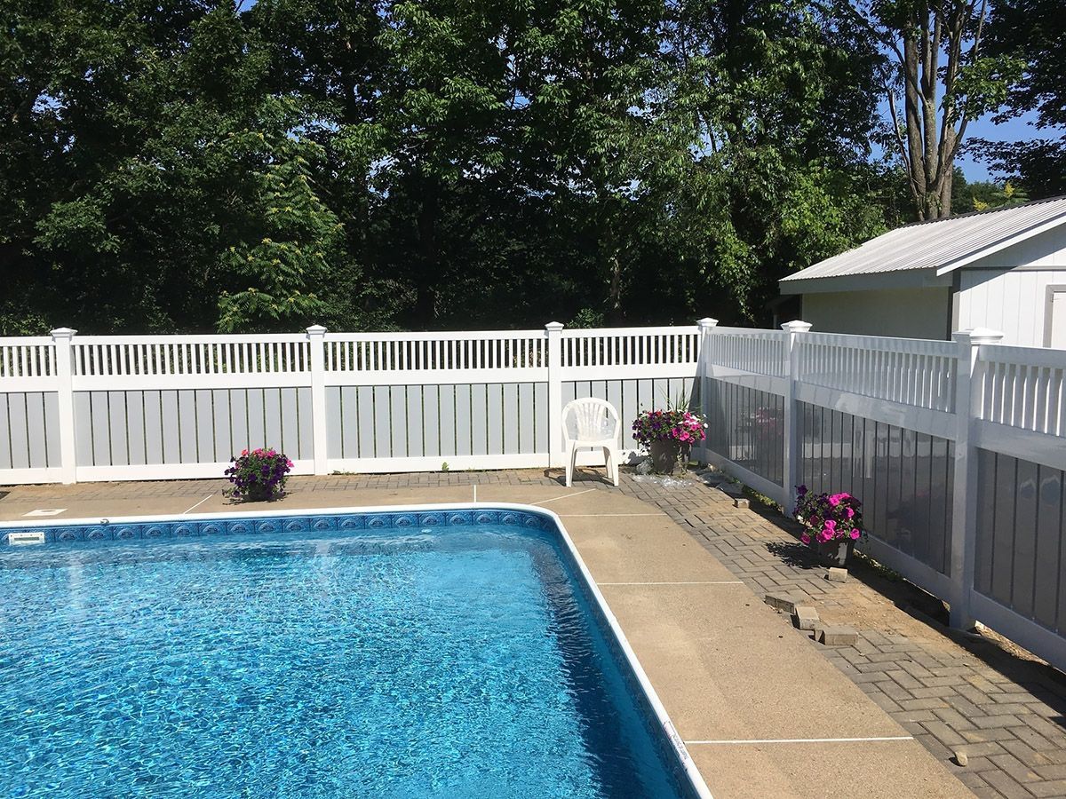 Swimming pool bordered by a white fence. Flowers in pots and a white chair are visible along the edge.
