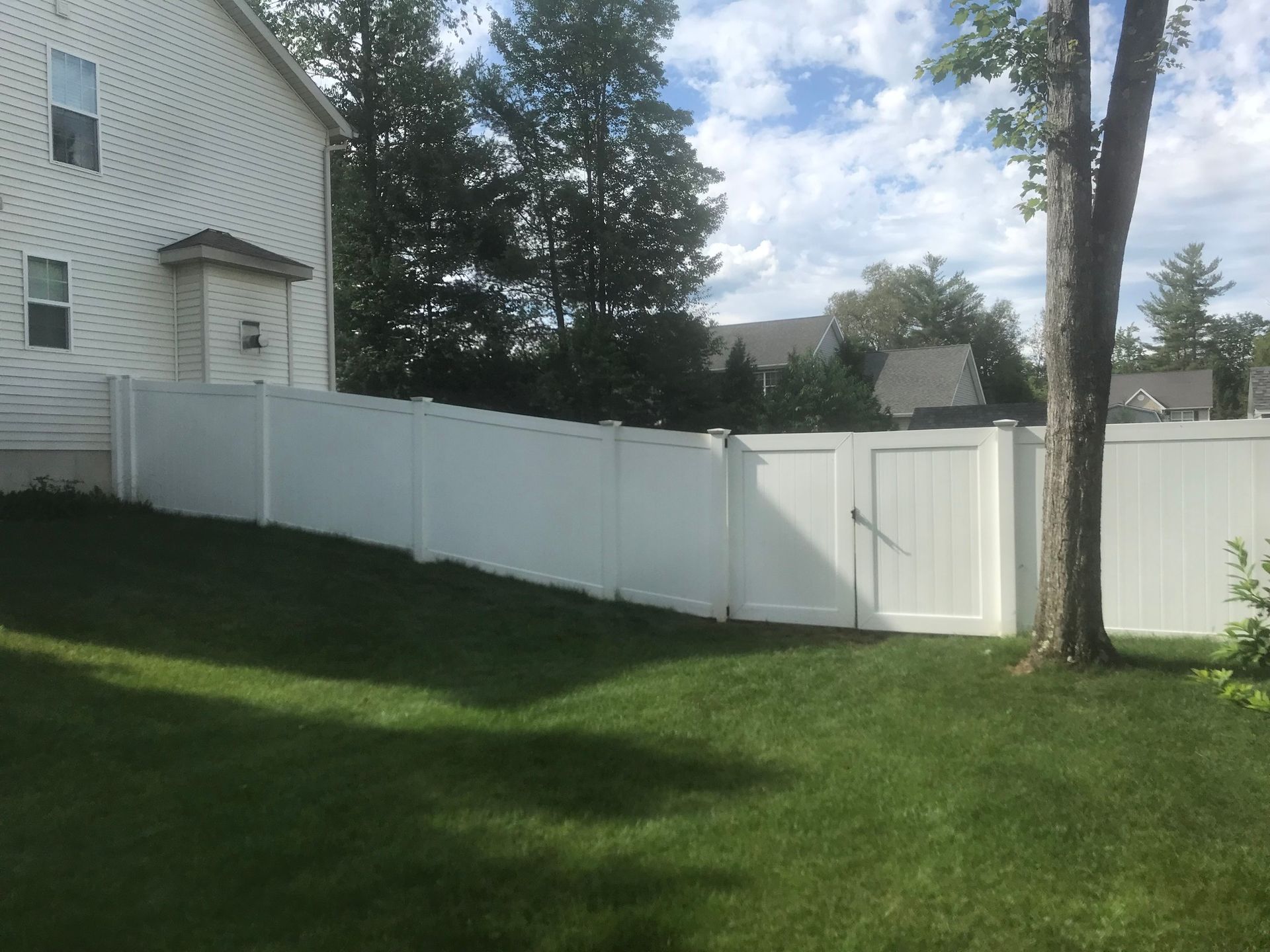 White vinyl fence encloses a green lawn, with a gate and a house in the background.