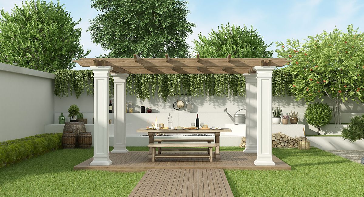 Outdoor dining area with wooden pergola, white columns, table set for meal, and lush greenery.