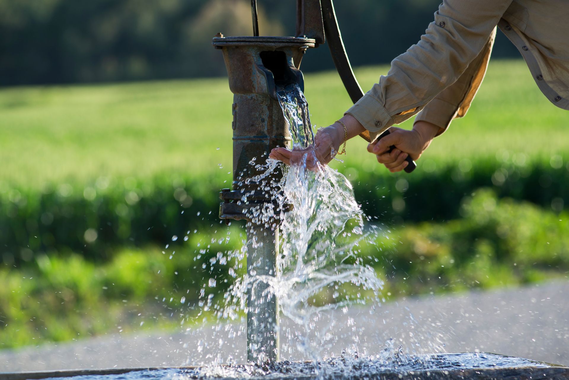 Hands collecting flowing water from a manual outdoor hand pump.