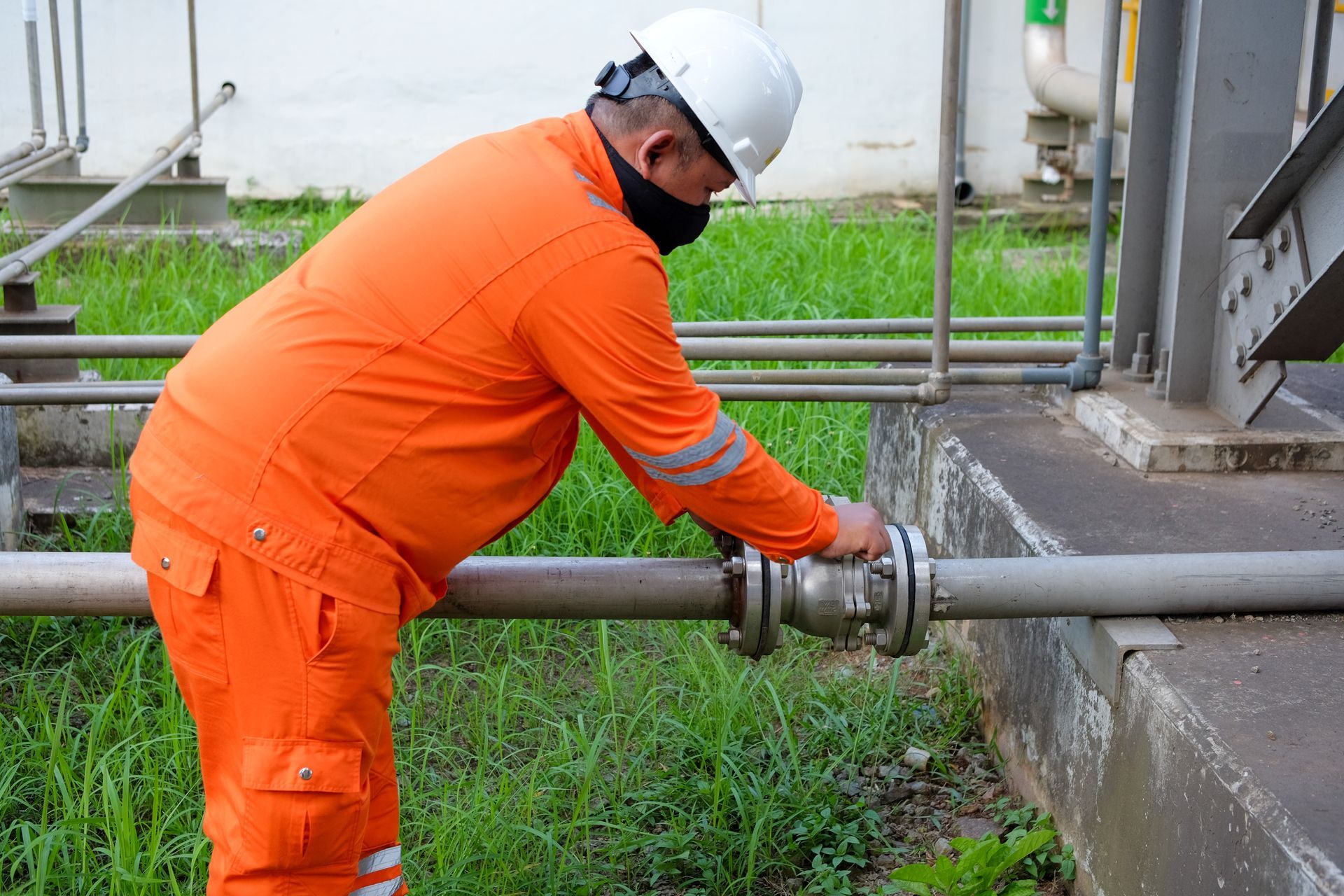 Worker inspecting water pipe valve outdoors.
