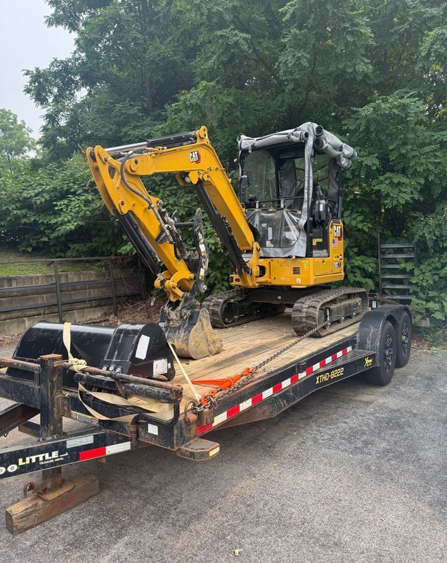 Yellow excavator on a trailer parked outside with trees in the background.