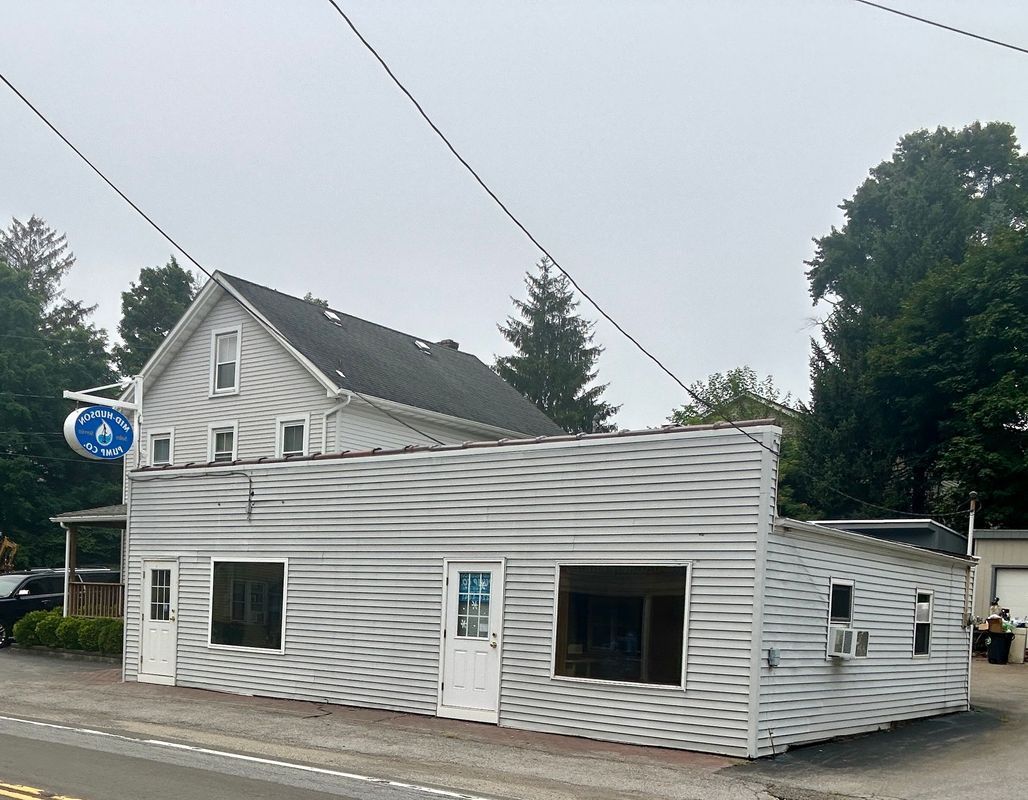 Grey-sided commercial building with open windows and a two-story residential section; overcast day.