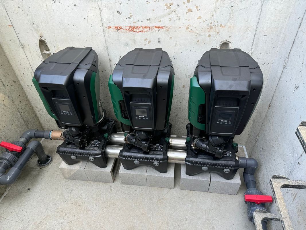 Three black and green irrigation control boxes, with plumbing, in a concrete enclosure.