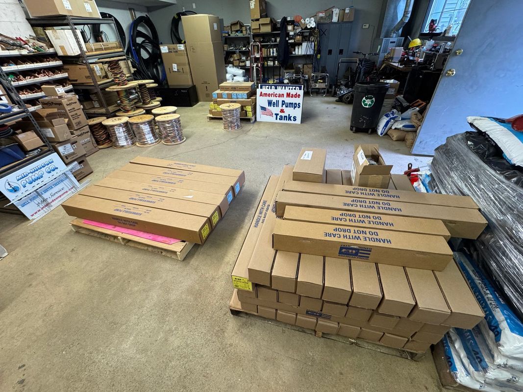 Boxes and packages stacked in a cluttered warehouse. Pallets of boxes on the floor; other items are in the background.