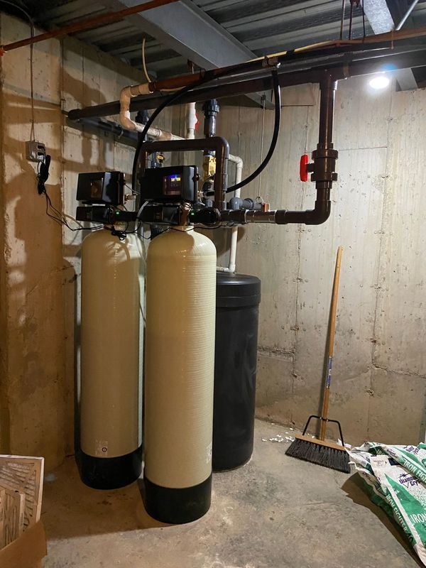 Water filtration system in a basement setting with two tall beige tanks and black piping.