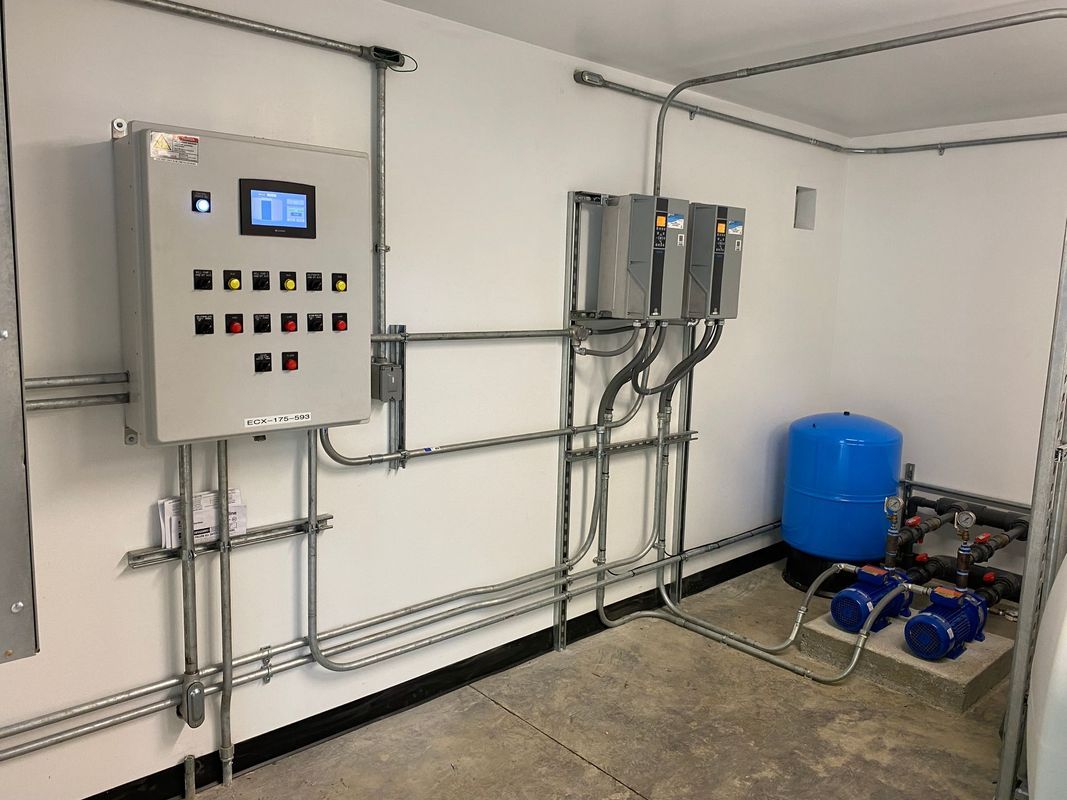Electrical control panel and equipment in an indoor setting. Gray panels, blue pressure tank, silver conduits.