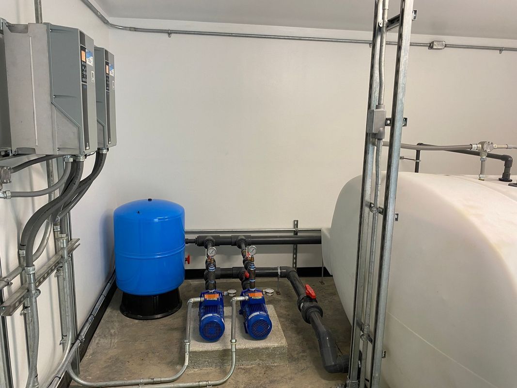 Water pump room with blue pressure tank, two blue pumps, and white tank.