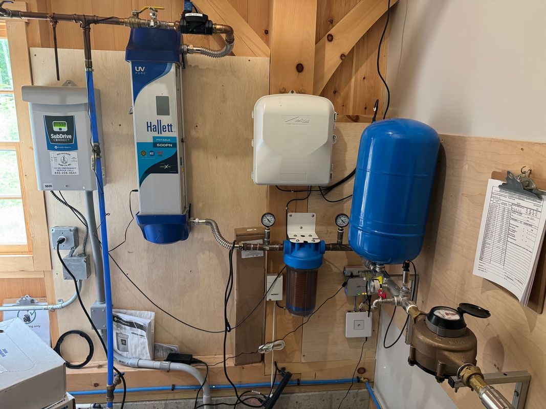 Water filtration and pressure system on wooden wall. Includes tanks, filters, gauges, and electrical components.