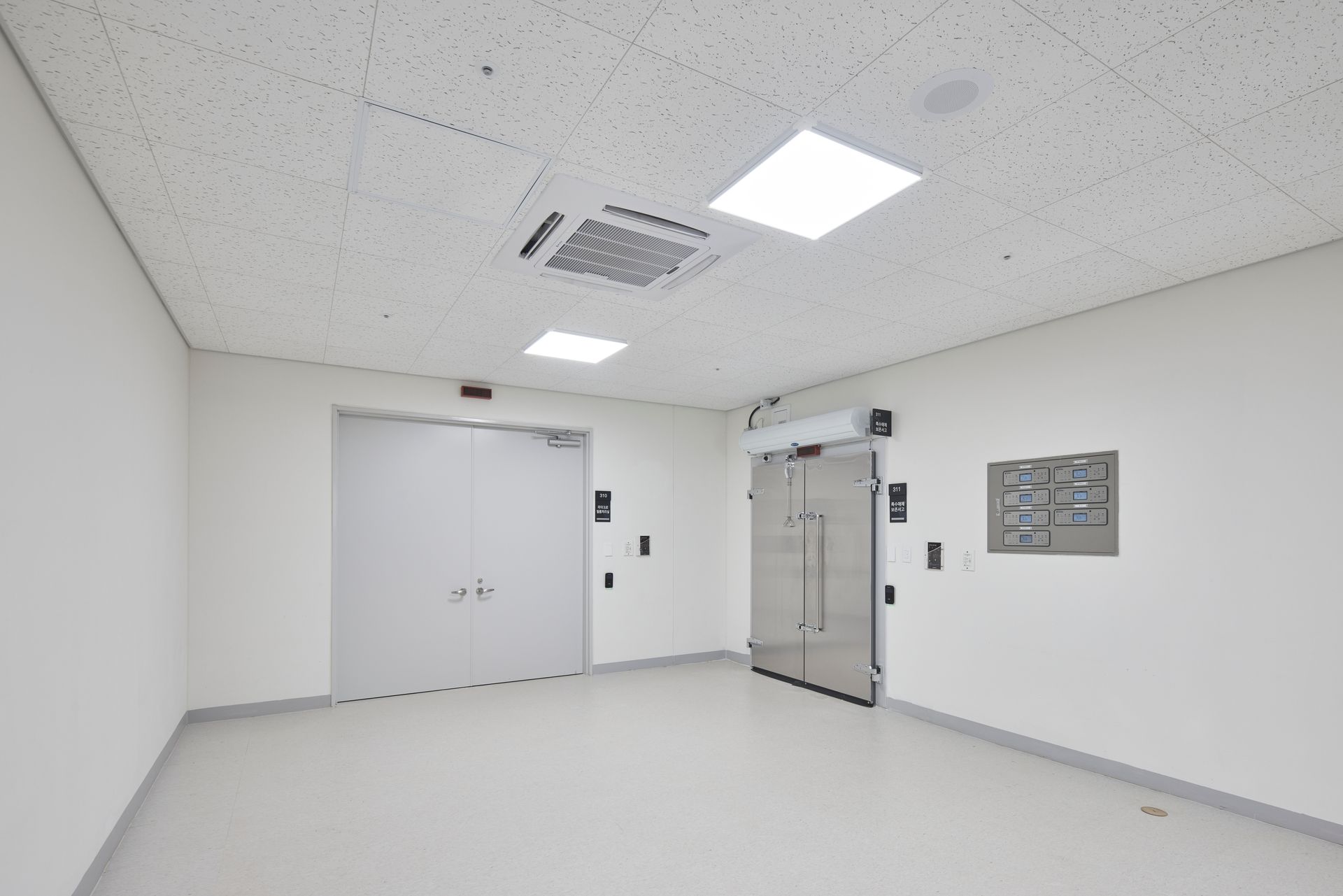 View of the empty interior of a white cold room with doors visible.