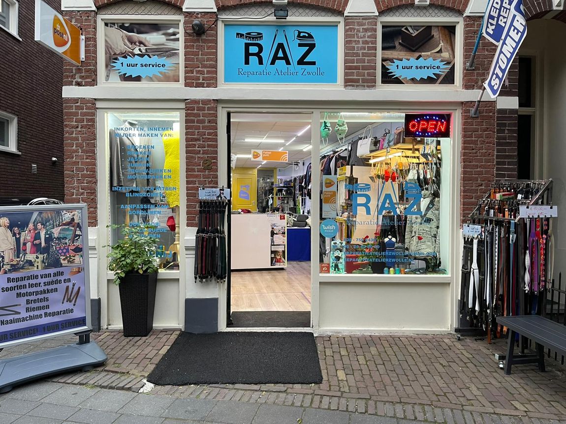 Winkelpui van een RAZ-winkel met een blauw uithangbord, bakstenen gevel en kledingdisplays in de etalages en buiten.
