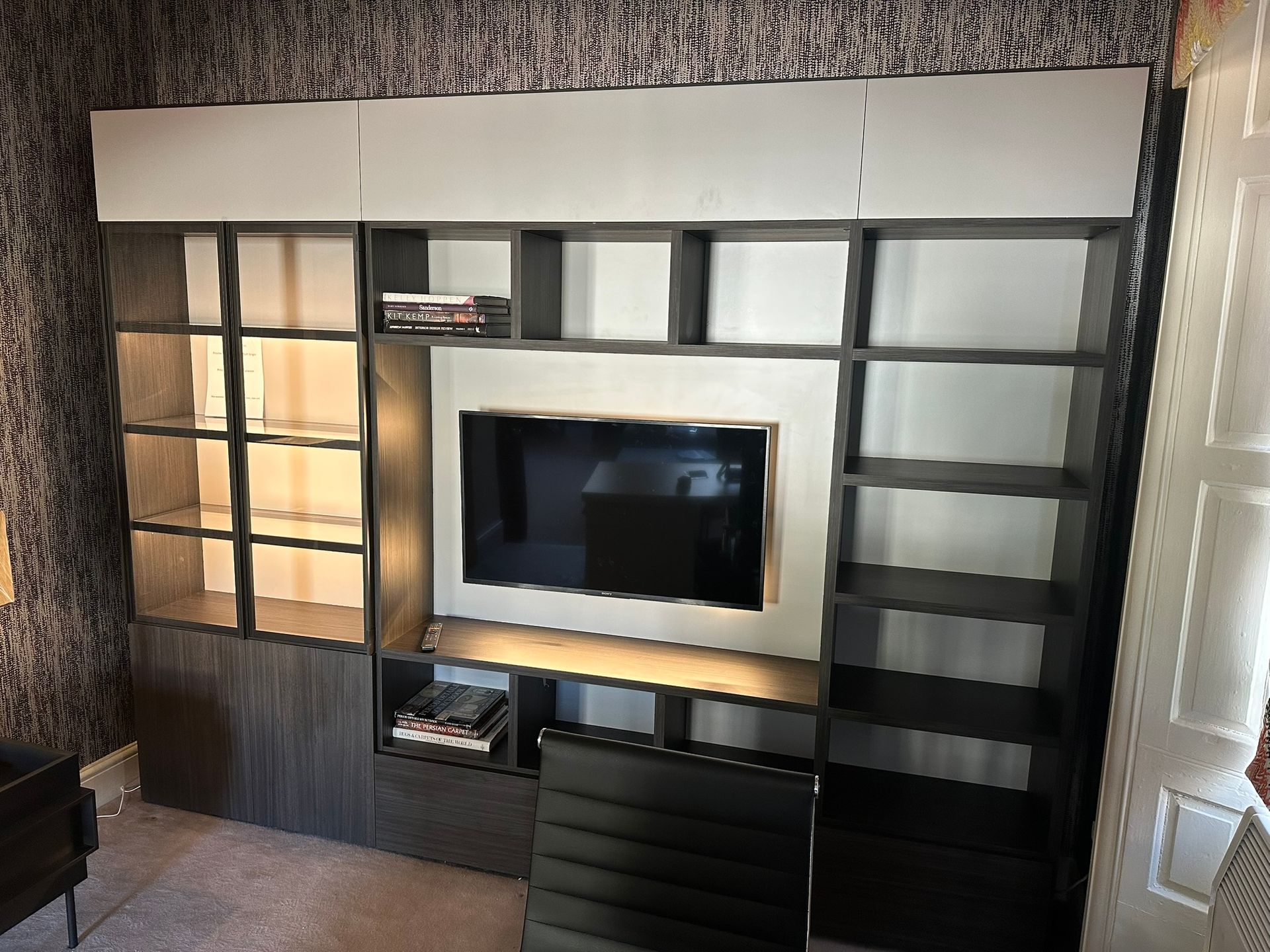 A large, dark-wood wall unit with open shelves, a central television, and top storage cabinets in a patterned room.