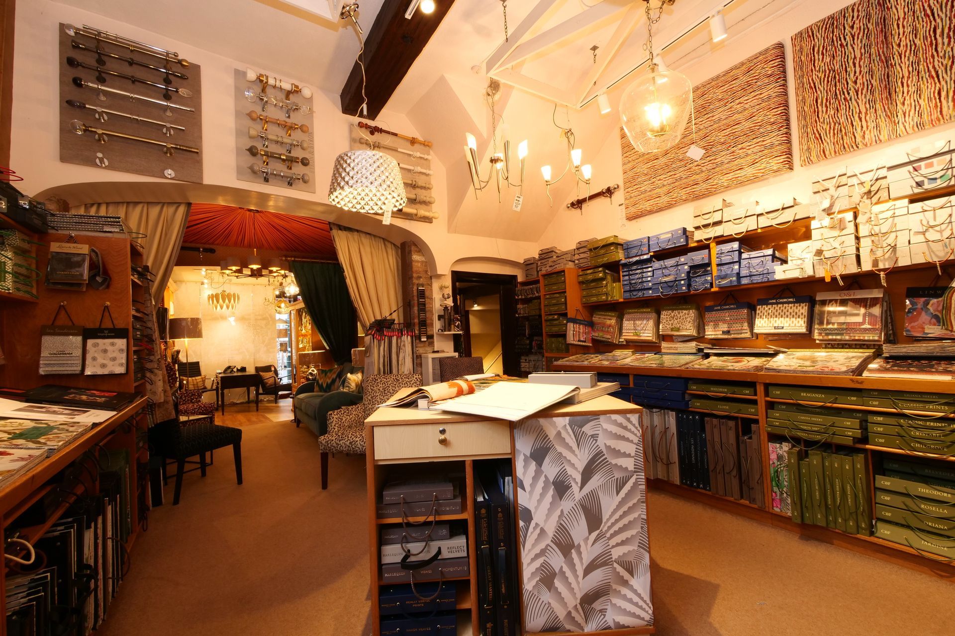 An interior view of a fabric and wallpaper design shop with shelves of samples, rolls of fabric, and drapery hardware.
