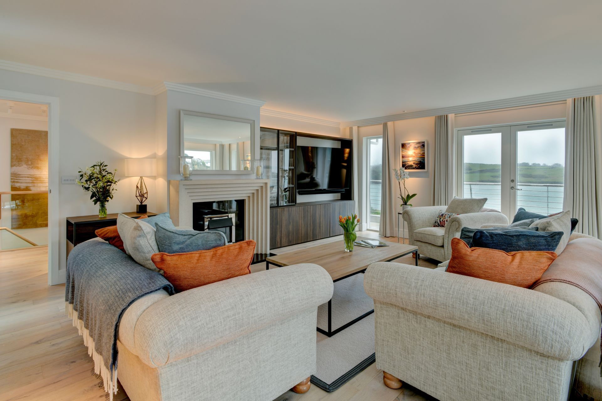 A cozy, light-filled living room featuring two textured cream sofas with orange cushions facing a wooden coffee table.