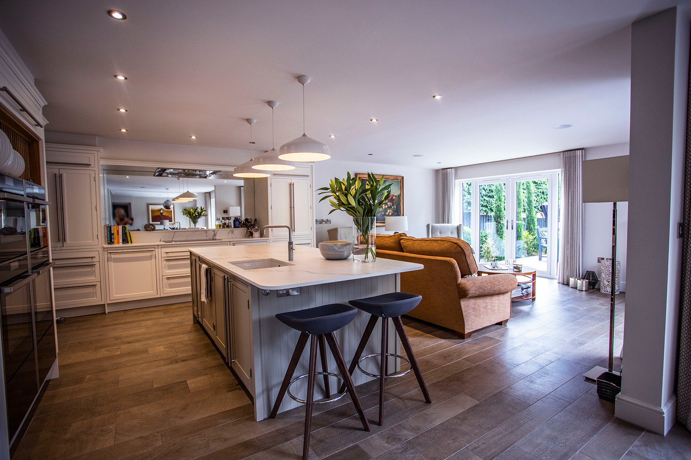A modern, open-plan kitchen and living room featuring a marble-topped island with two bar stools and a cozy brown sofa.
