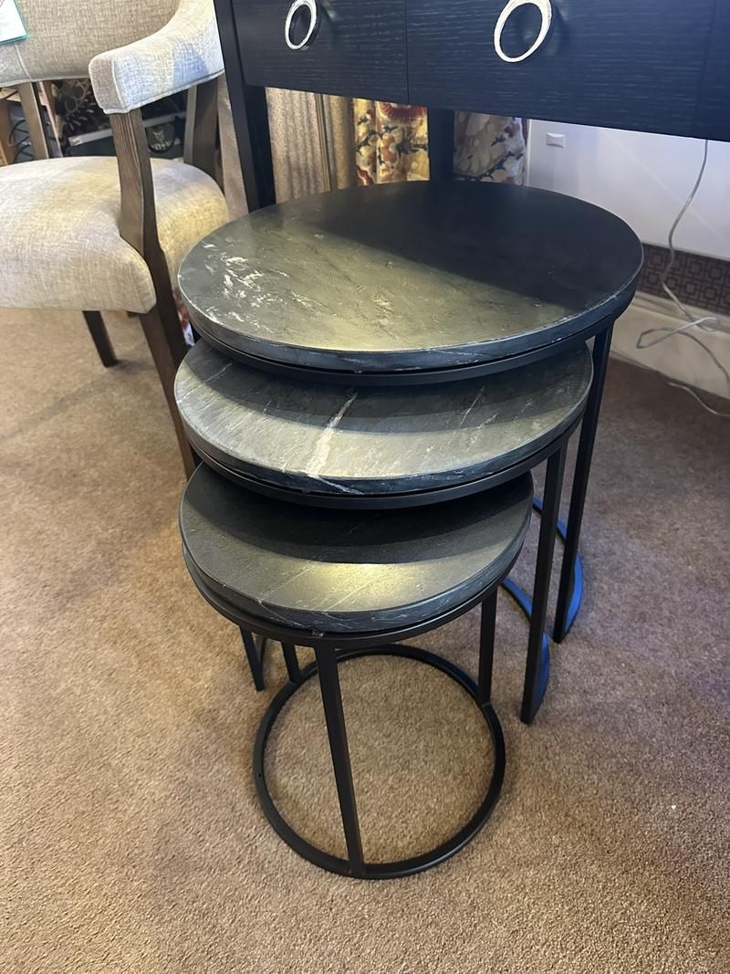A set of three tiered round tables with black marble tops and black metal legs on a carpeted floor.