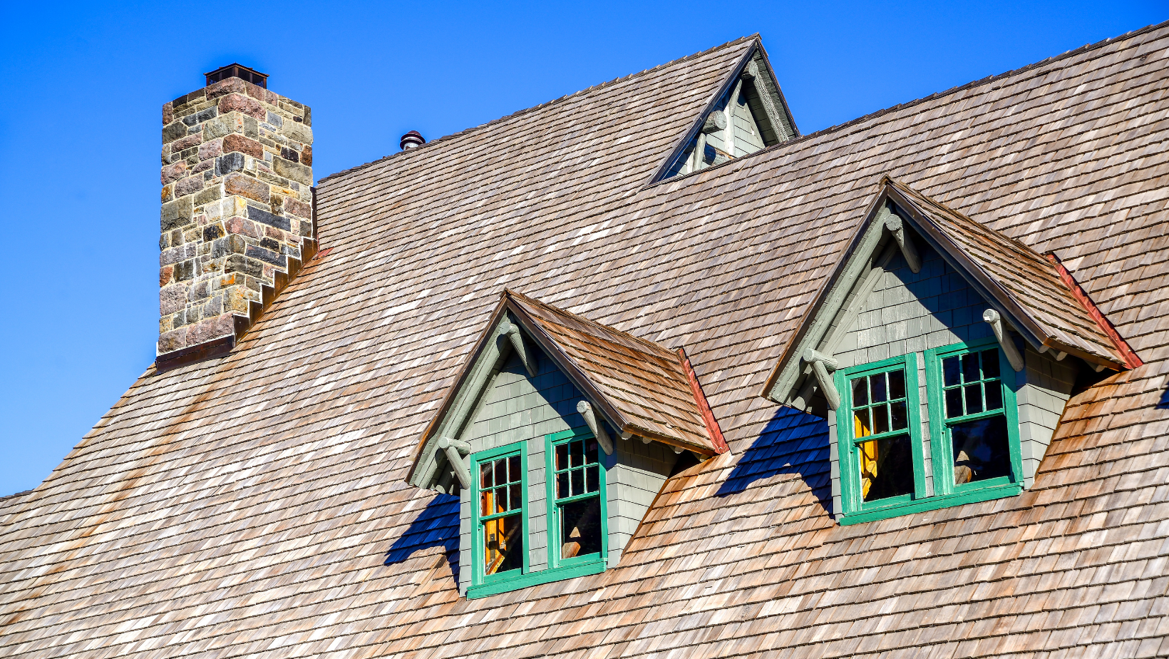 The roof of a house with two green windows and a chimney.