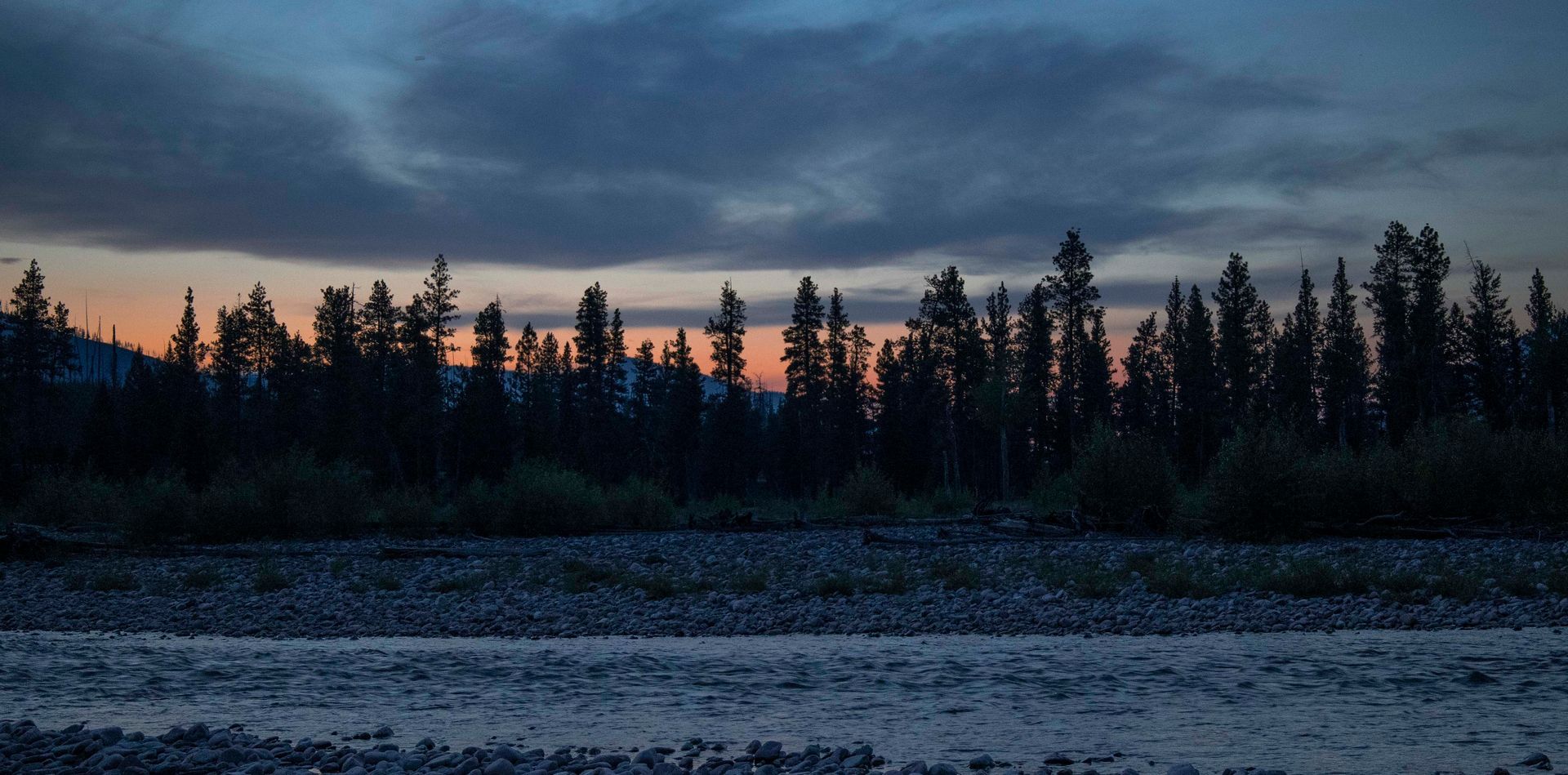 A river with trees in the background and a sunset in the sky.