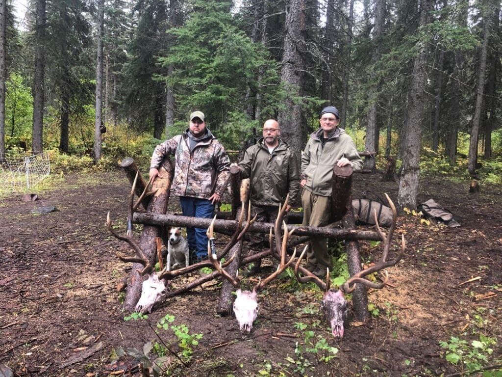 Three men showing of deer skull trophies