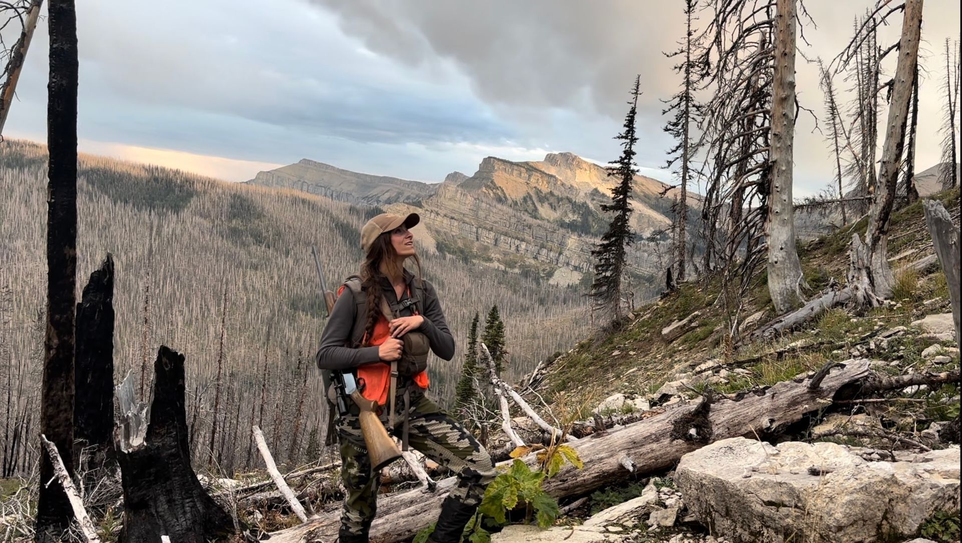 A person is sitting in a field looking at a mountain range.