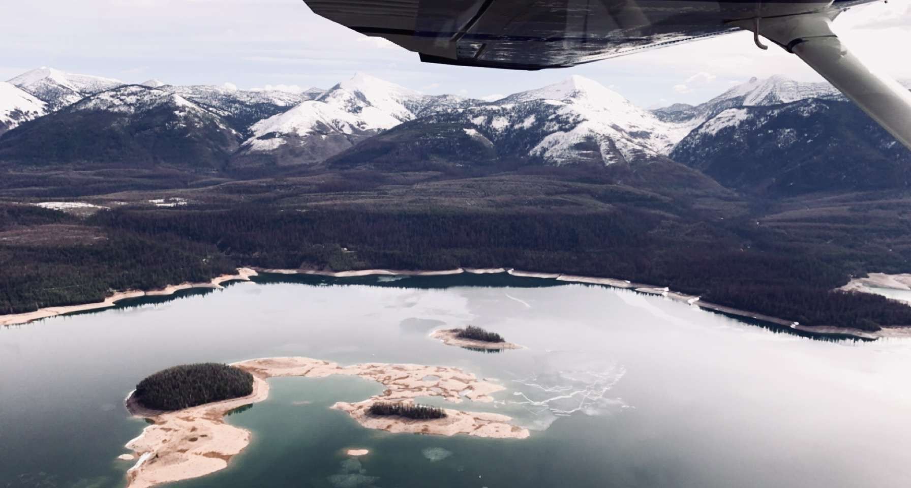 A plane is flying over a lake with mountains in the background
