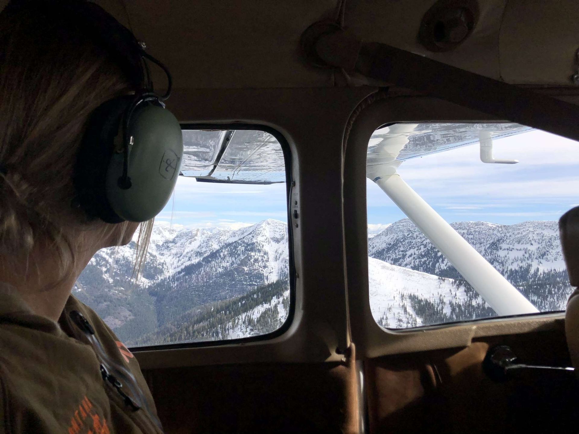 A woman wearing headphones looks out the window of a plane