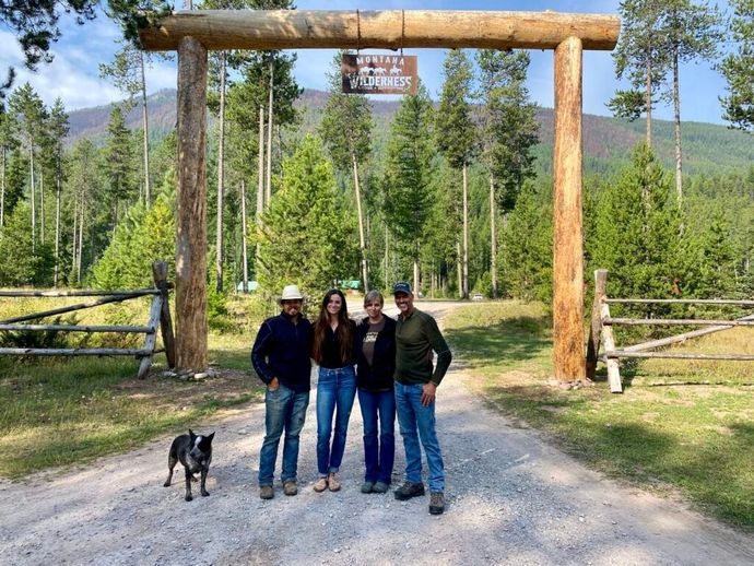A group of people and a dog are posing for a picture in front of a wooden gate.
