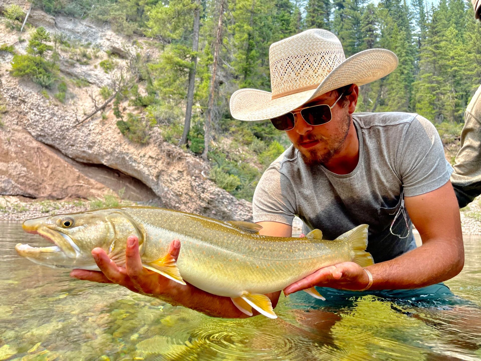A man in a cowboy hat is holding a large fish in his hands.