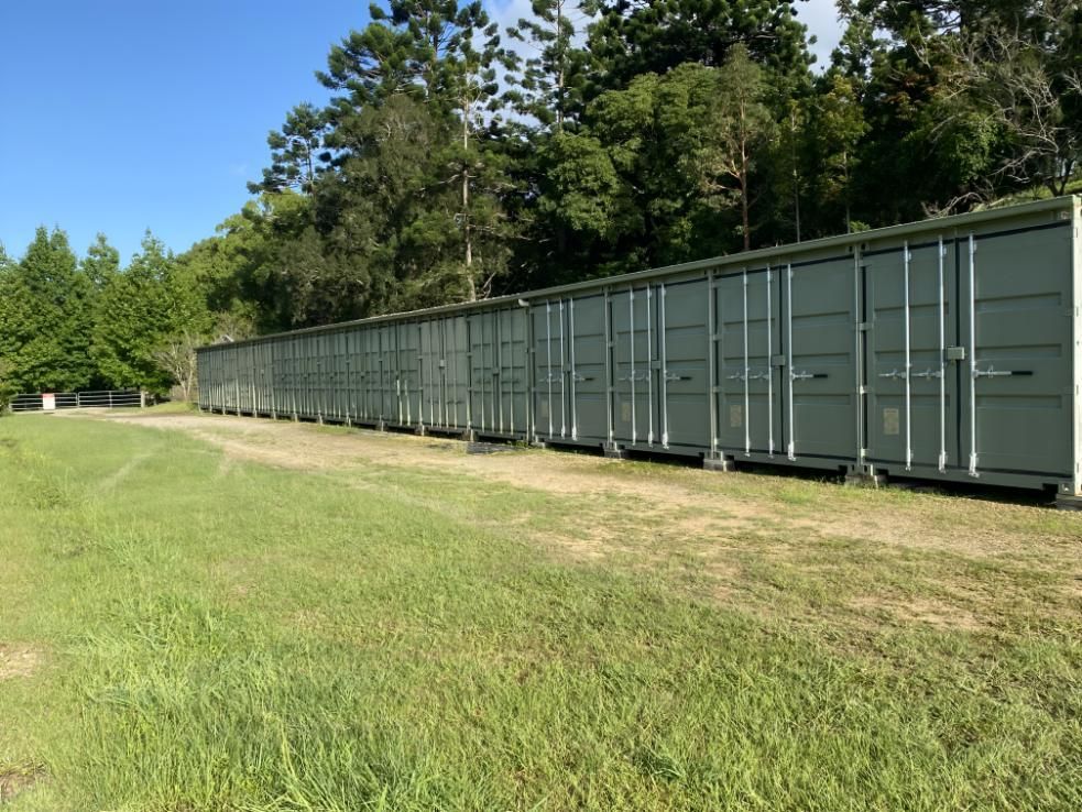 A Row Of Storage Containers Are Lined Up In A Grassy Field — Byron Storage Services In Myocum, NSW