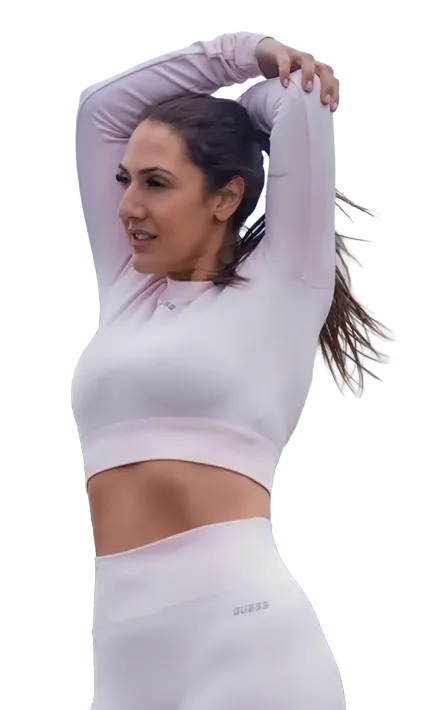 Woman in a light lavender athletic outfit stretching with arms raised overhead outdoors.