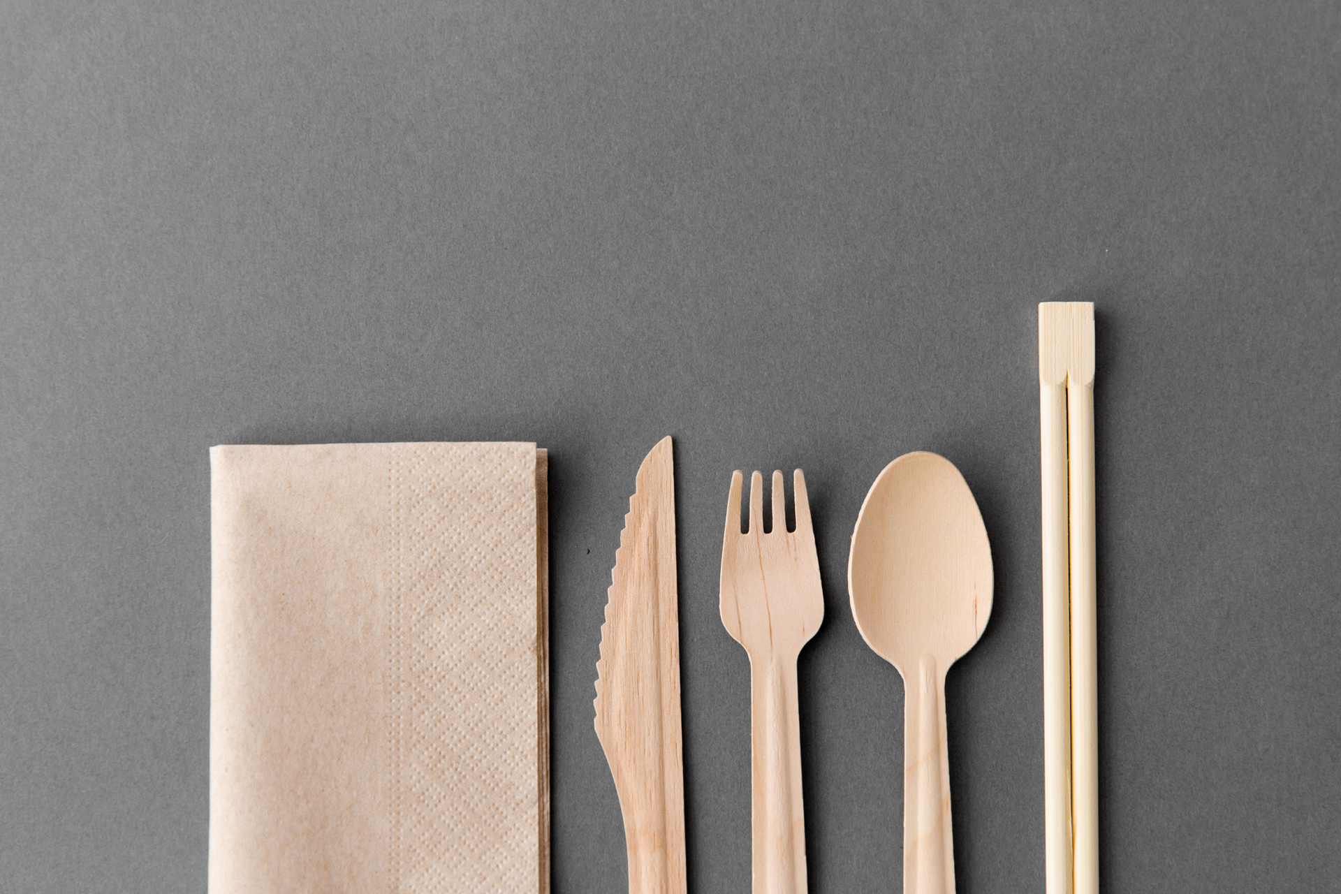 Napkin, wooden knife, fork, spoon, and chopsticks on gray background.