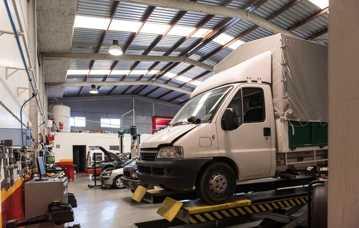 A white truck elevated on a lift inside a well-lit automotive repair workshop with multiple work bays.