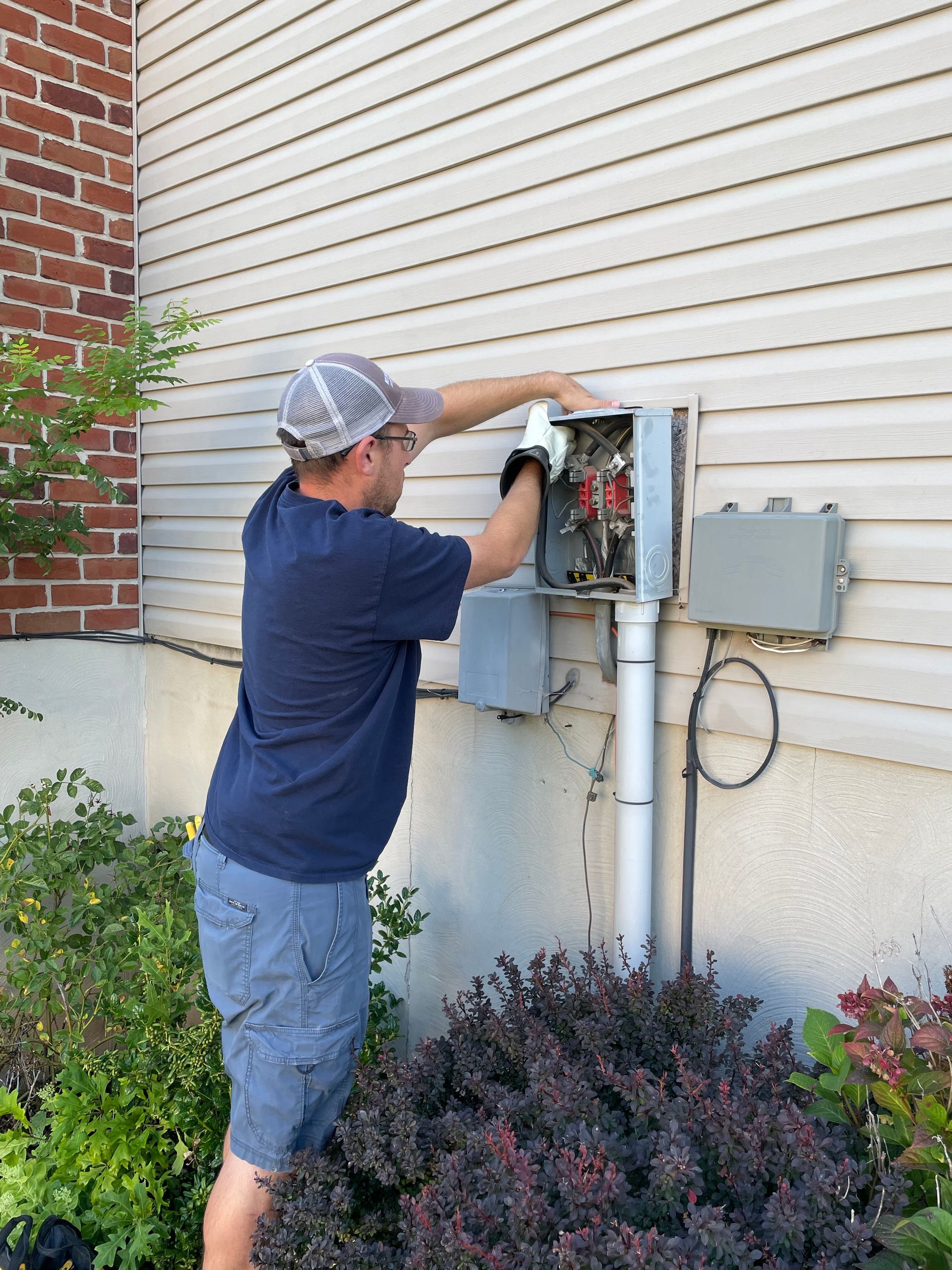 A man is working on an electrical box on the side of a house.