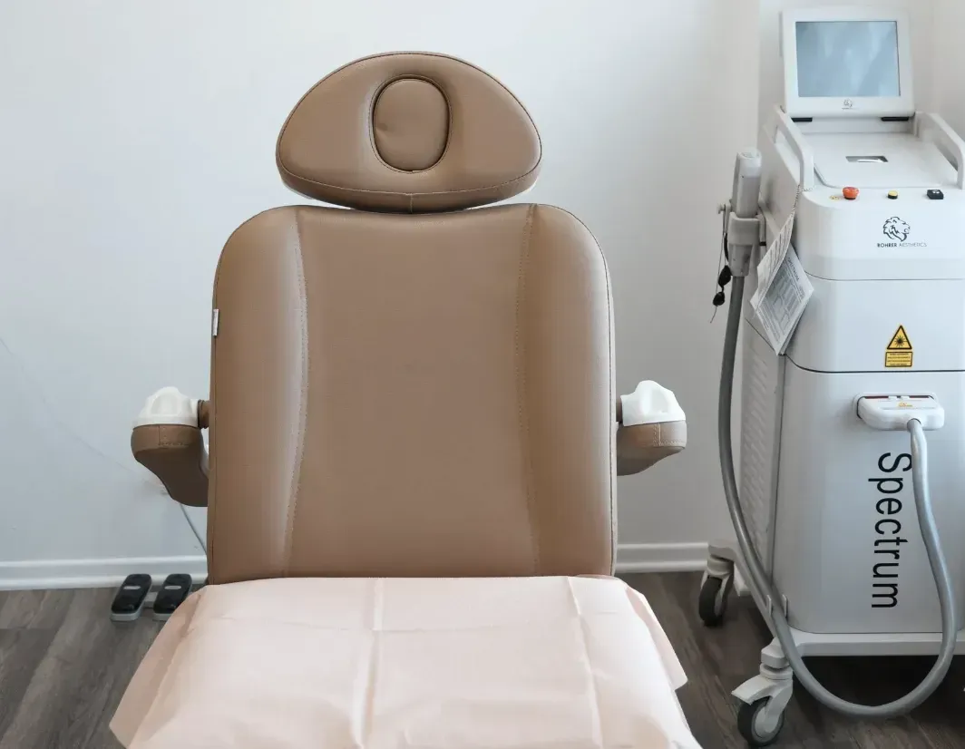 Tan medical chair with headrest and armrests, next to a Spectrum laser machine in a clinic setting.