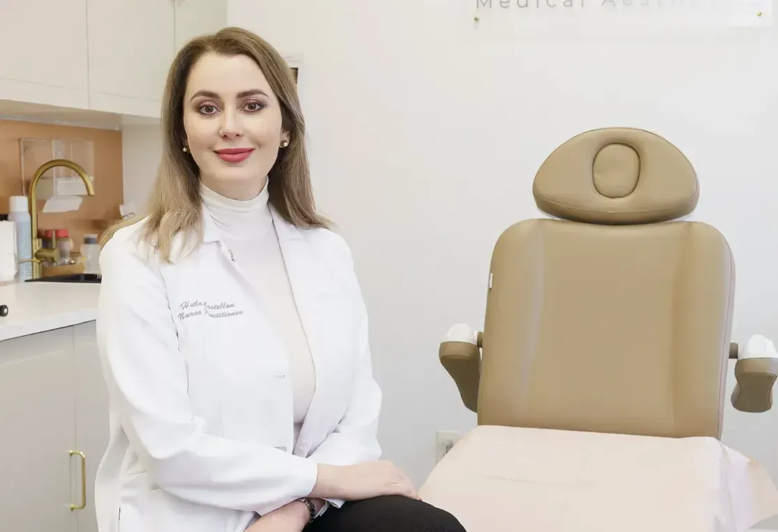 Hula Castellon, FNP, MSN, and owner of Uplifted Aesthetics sits in front of medical chair in at Uplifted Aesthetics.