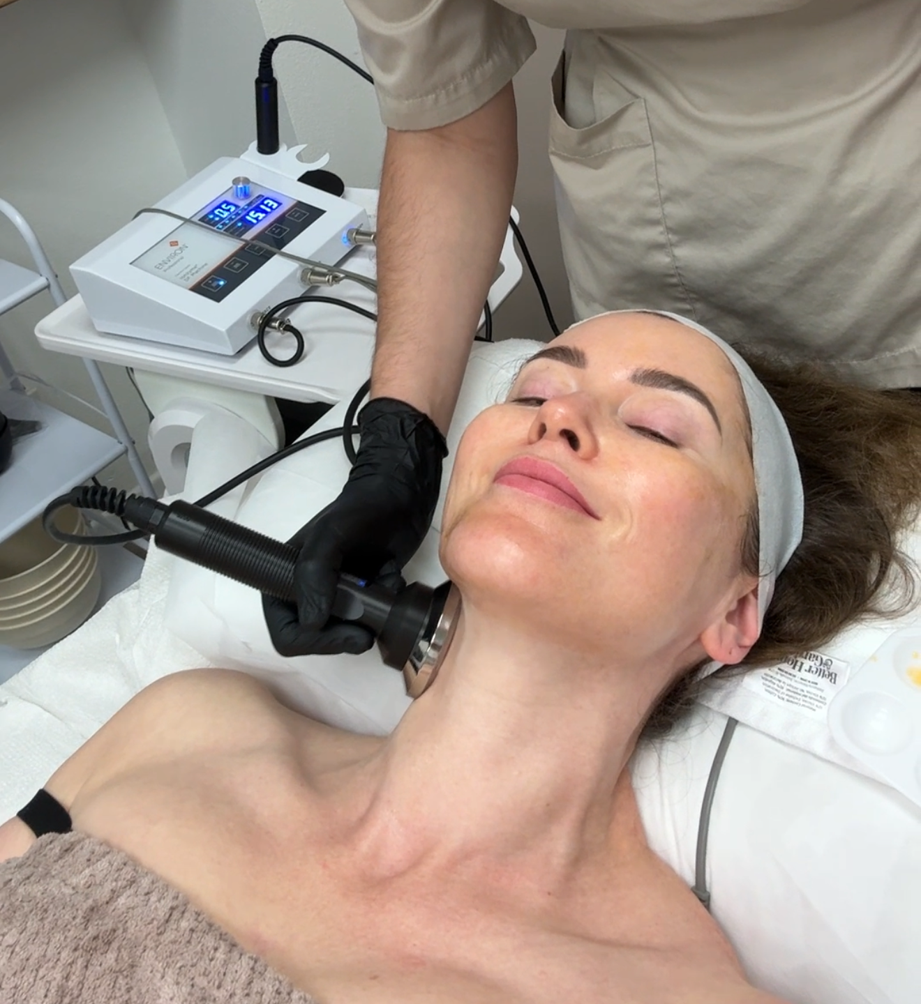 Woman receiving skin treatment on her neck; machine and gloved hand visible.