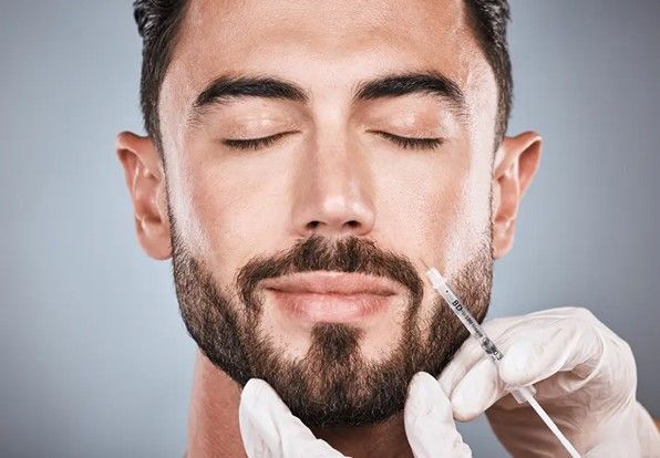 Man receiving injection in the face. A syringe is held near his lips. He has his eyes closed.