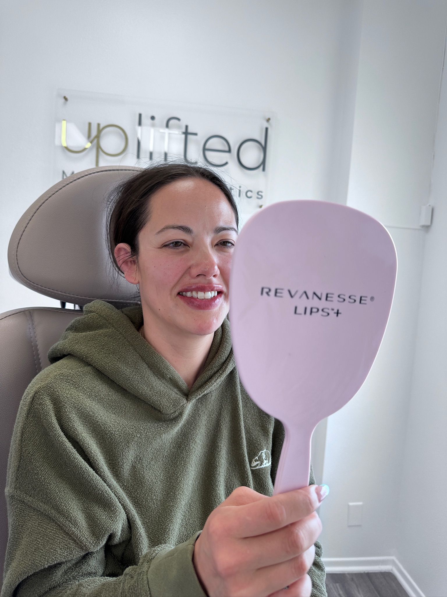 Woman holding a pink mirror, smiling, in a medical office; the mirror says 