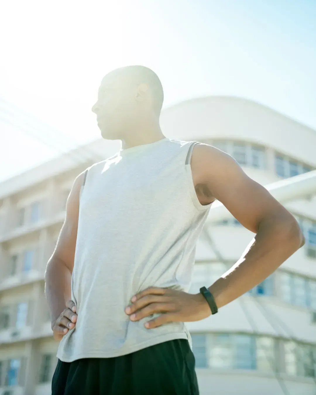 Man in athletic wear with hands on hips, looking away, in front of a building.