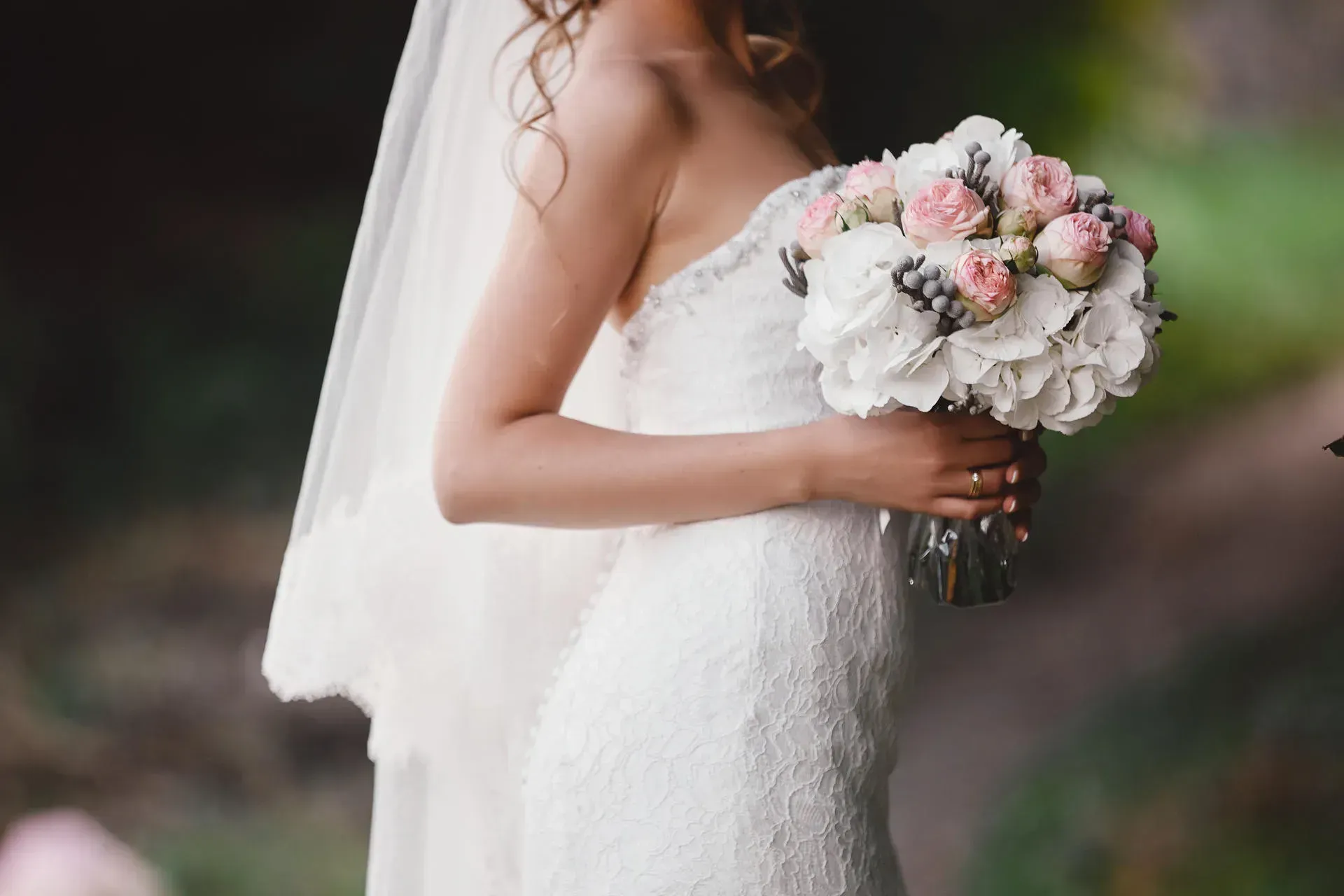 Bride in a white strapless wedding dress, holding a bouquet of pink and white flowers; veil.