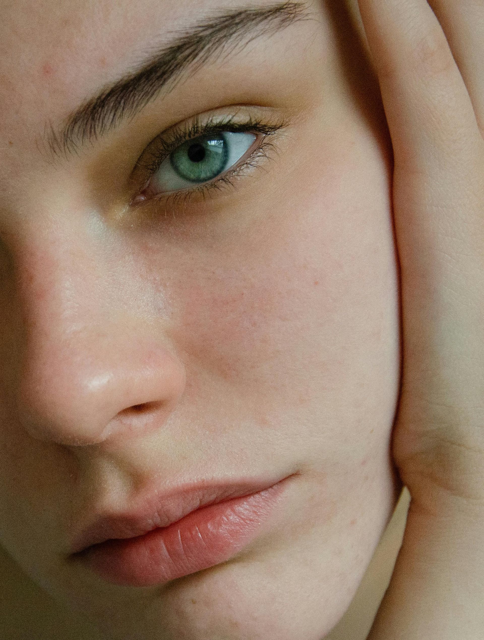 Close-up of a person with light blue eyes, fair skin, and a contemplative expression, face framed by hands.