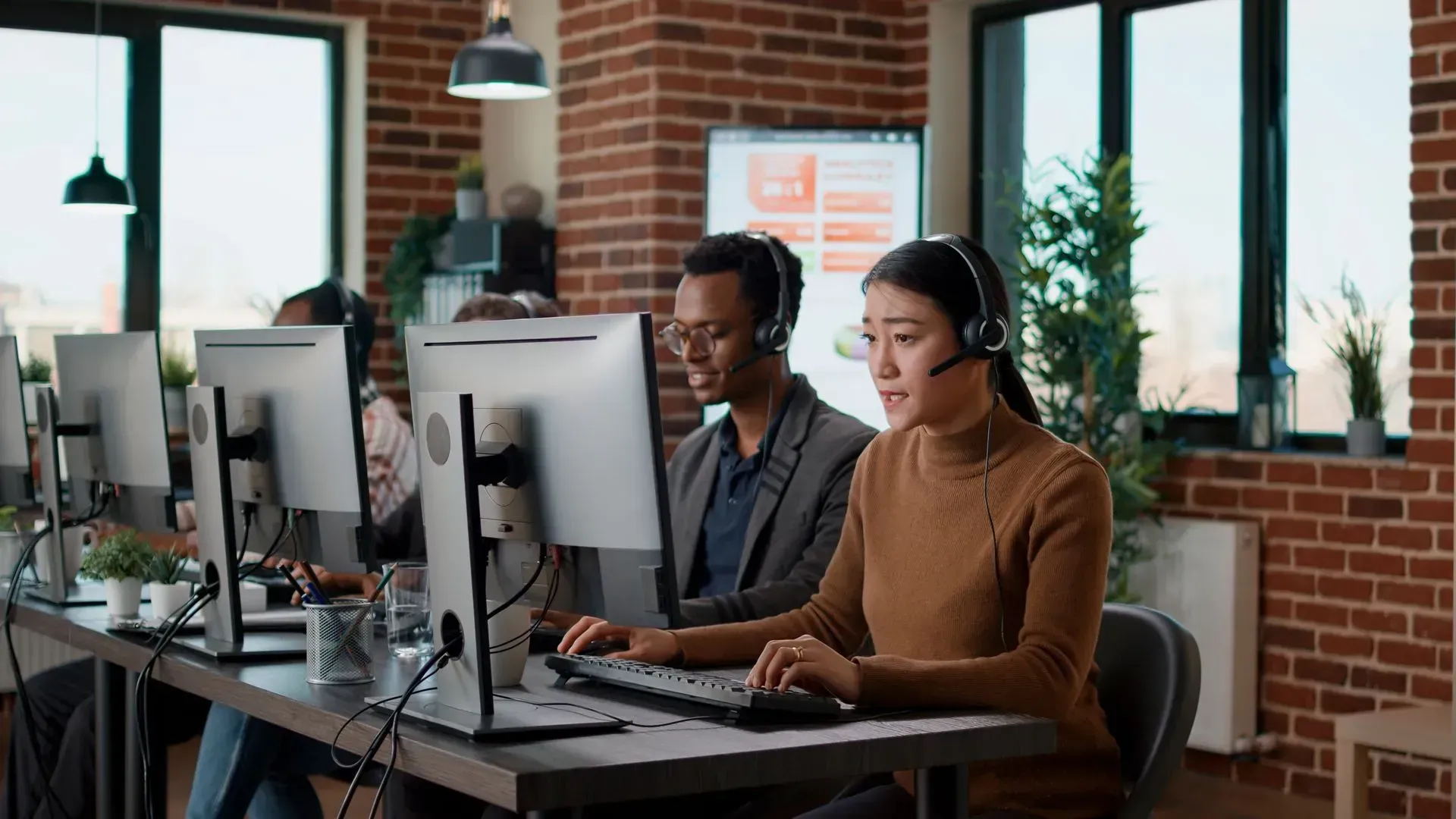 Professional customer service representatives in an office, wearing headsets and working at computers.