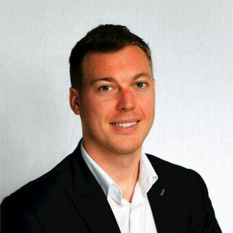 Headshot of smiling man in navy suit and light blue dress shirt against gray background.