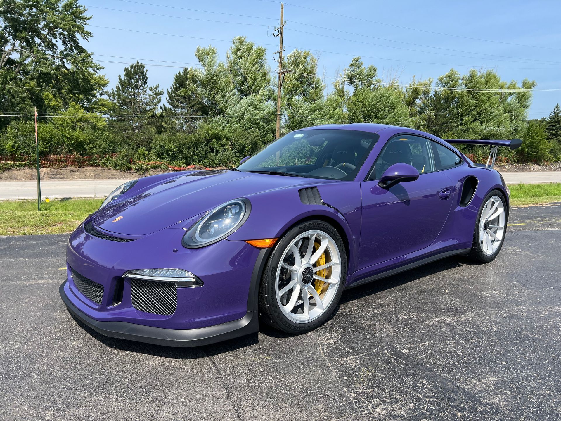 Purple Porsche 911 GT3 RS sports car parked on asphalt, yellow brake calipers, sunny day.