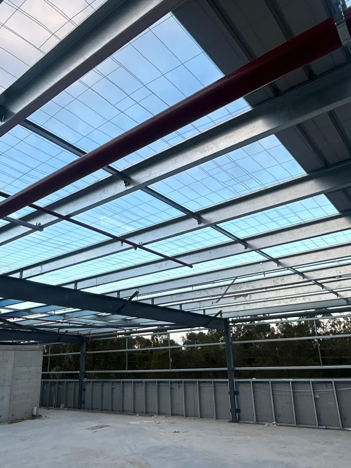 Open-air construction with steel beams and a translucent roof over an empty concrete structure